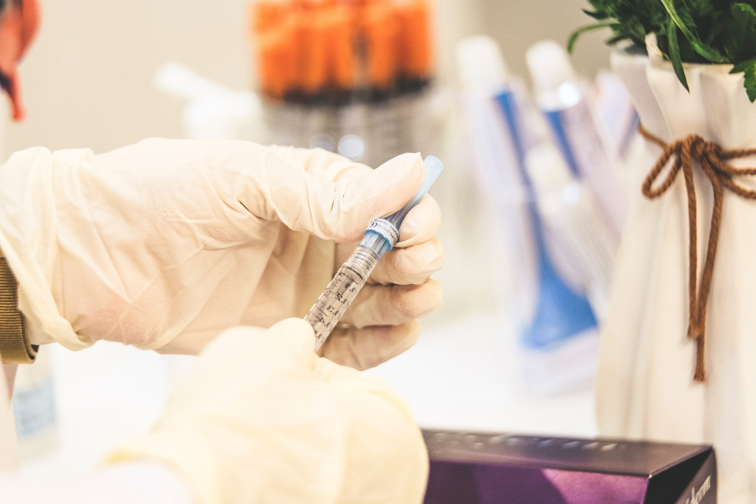 vaccination Hands in medical gloves hold an injection. THere a plant to the side and extra injections in the background