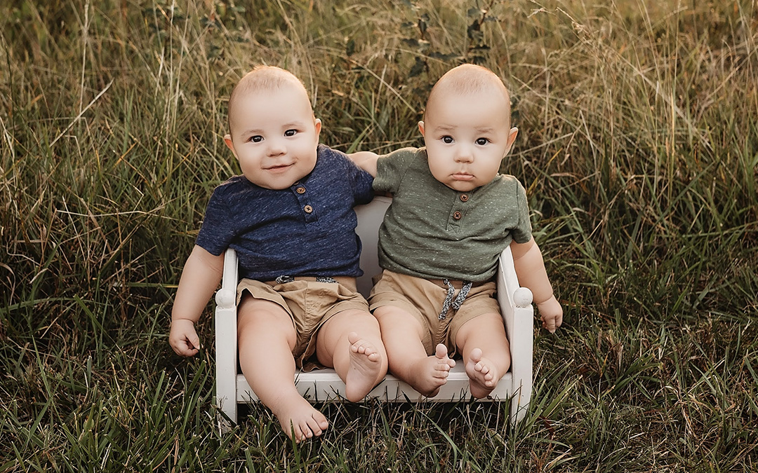 Infant TTTS survivor twin boys sit in a tiny chair outside to post for a photo
