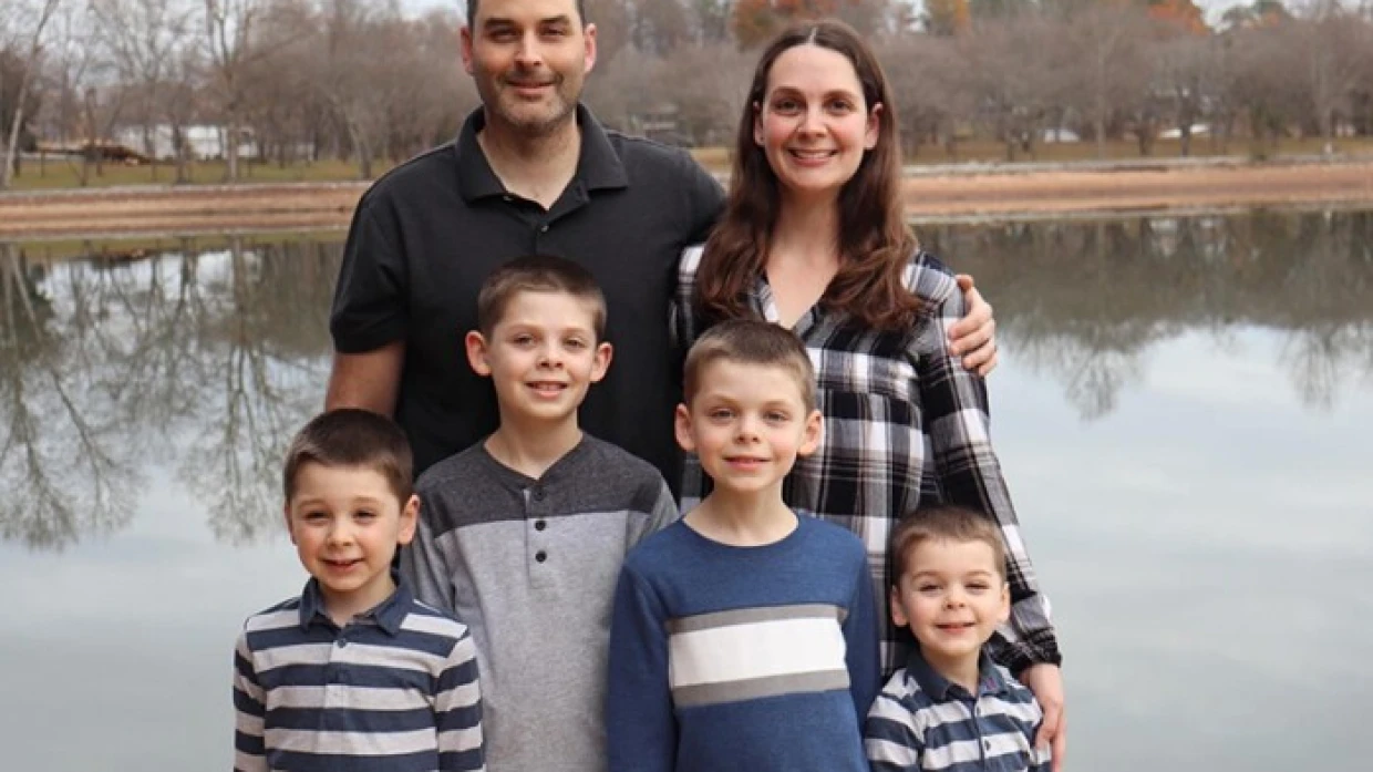 Mom, dad and four boys stand by a lake, smiling
