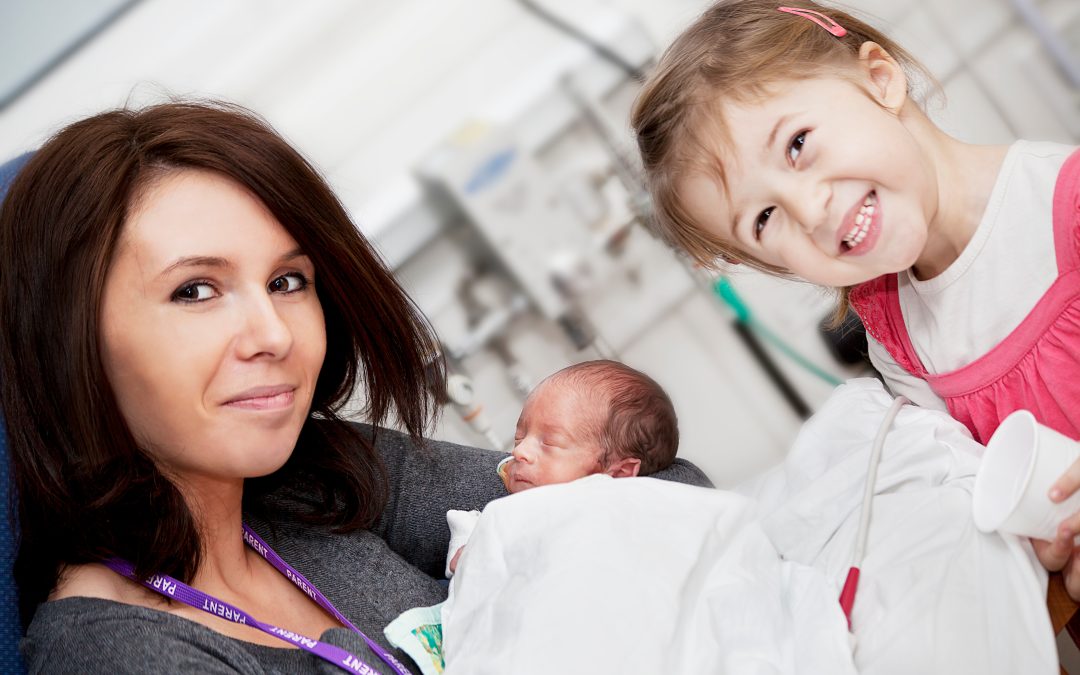 Mom holds newborn baby in a Maternal-Fetal Surgery Center, following treatment, with toddler smiling beside them.