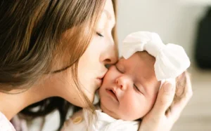 Mom kisses peacefully sleeping baby on the cheek and cradles her in her hands. 