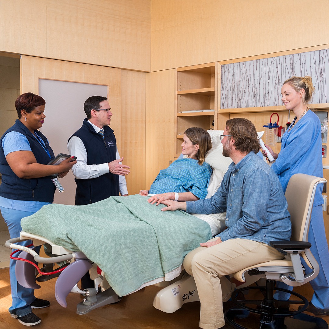 Pregnant woman dealing with a high-risk pregnancy rests in bed while surrounded by medical and non-medical supporters