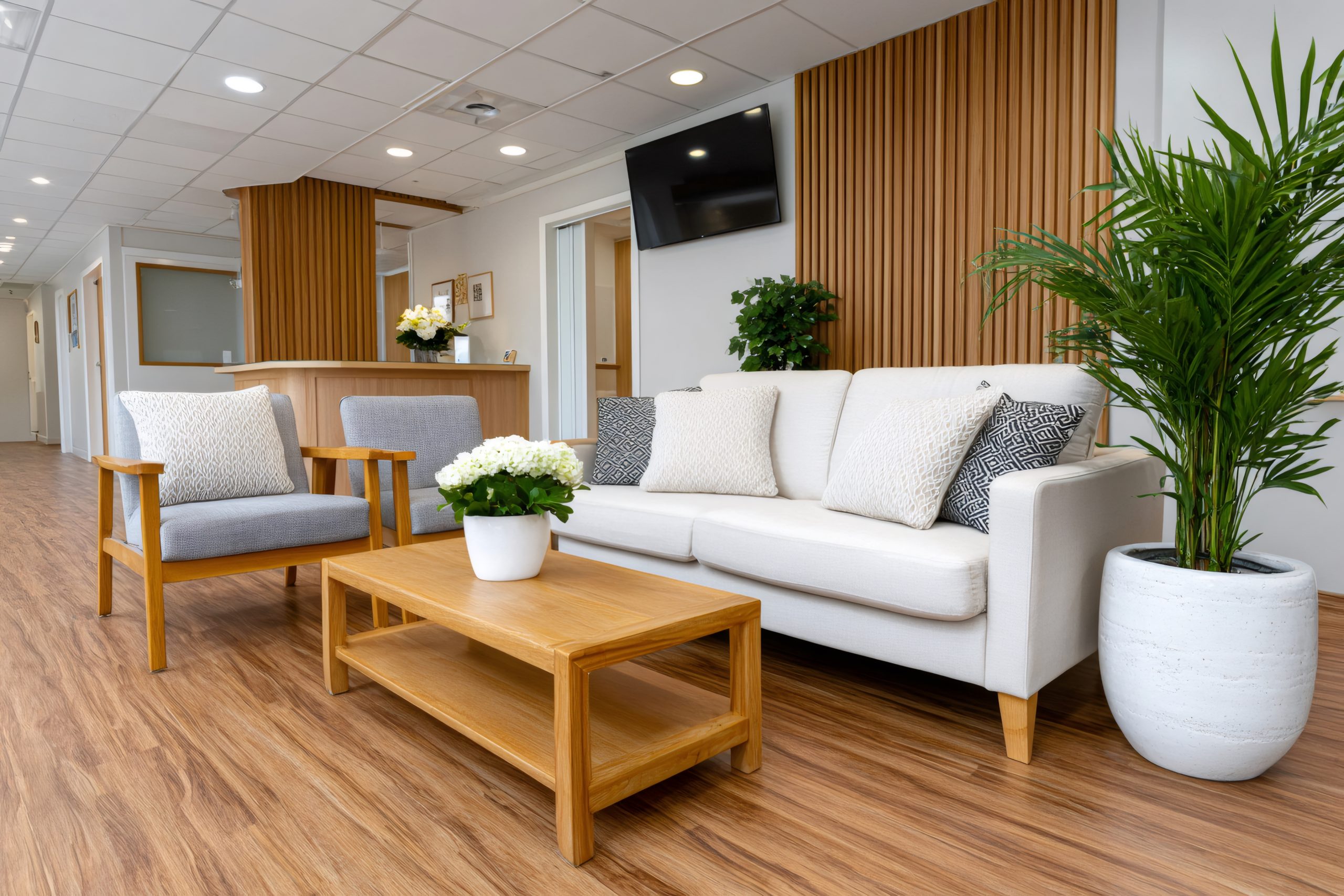 Modern waiting room with comfortable sofa, armchairs and wooden furniture welcoming patients A modern, comfortable waiting room in a hospital that is flooded with light and feels homey with couches and plants.