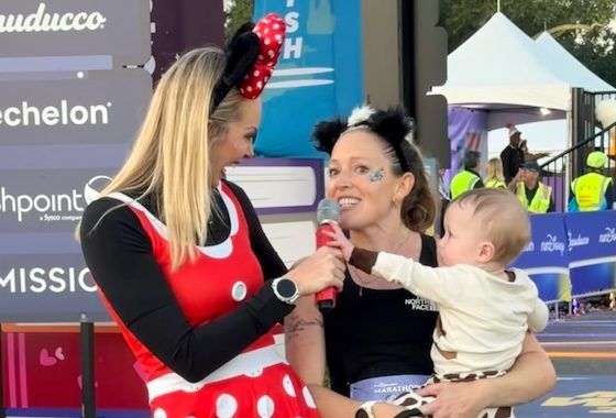 Funny Runner Disney (1) A woman wearing Mickey Mouse ears holds her toddler after running a race. She is being interview by someone in a minnie mouse costume.