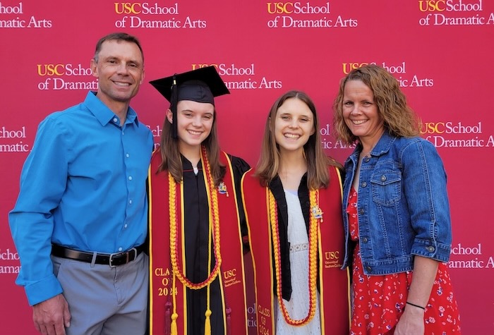 Mom and dad with twin daughters in graduation caps and gowns